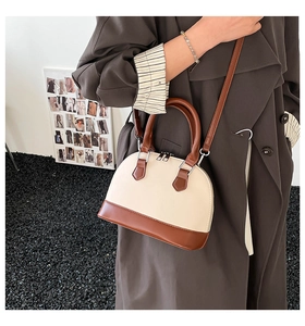 Detail of a beige and brown shell-shaped crossbody bag styled with a brown trench coat