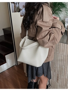 Detail of off-white lychee grain leather tote bag with wide strap worn by model
