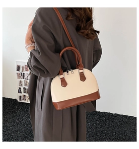 Detail of a two-tone shell bag in cream and brown leather worn over a dark winter coat