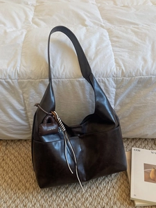 Sac hobo rétro marron foncé en cuir texturé avec breloque de marque sur tapis tressé