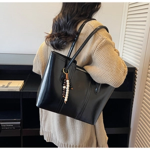 Side view of a black glossy tote bag with stylish beaded pendant on a female model