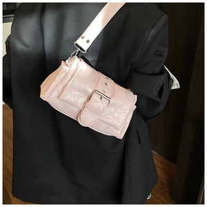 Detail of light pink crossbody bag with wide buckle strap worn over a black blazer