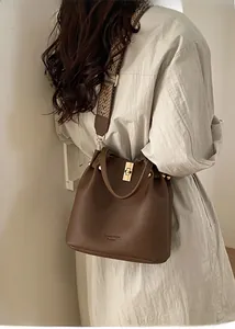 Detail of brown litchi leather bucket bag featuring a woven strap and gold metal lock