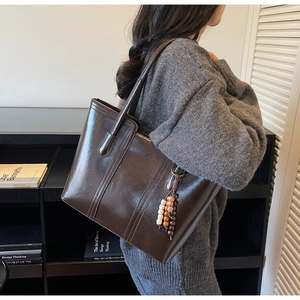 Close-up of a large dark brown leather tote bag featuring a decorative beaded charm detail