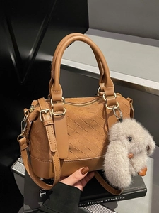 Brown woven Boston bag with plush rabbit charm and gold-tone hardware on dark background
