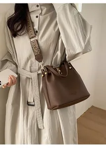 Detail of brown lychee grain leather bucket bag with wide jacquard shoulder strap and gold hardware