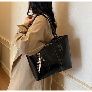 Detail of black glossy tote bag with stylish wooden bead pendant on slim leather straps