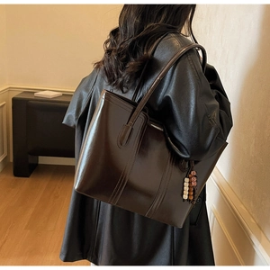 Detail of a large dark brown tote bag with oily leather finish and bead charm on model