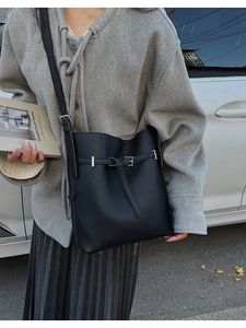 Detail of black pebbled leather bucket bag styled with a grey wool coat in a street scene