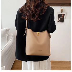 Detailed view of beige pebble leather shoulder bag with gold hardware on a female model