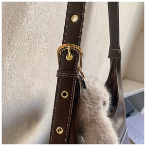 Detail of coffee brown tote with white stitching, gold buckle and plush charm