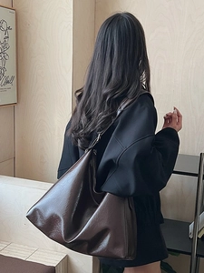 Minimalist deep brown faux leather bucket bag shown on model in a stylish indoor setting