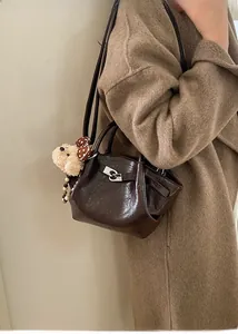 Détail du sac seau marron foncé avec cuir brillant et pendentif ours en peluche