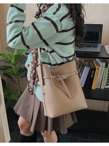 Close-up of light brown lychee grain leather bucket bag with metal buckle and shoulder strap