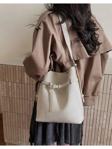 Detailed view of cream bucket bag with lychee grain texture and metal buckle belt