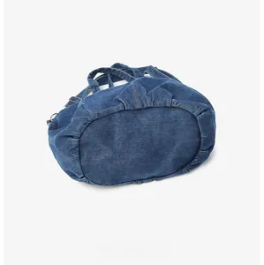 Detailed bottom view of large denim tote bag featuring reinforced pleats and metal rings