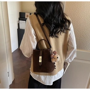Detail view of deep brown suede bucket bag with gold buckle and cute plush bear charm