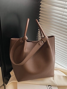 Brown lychee leather bucket bag with top handle and shoulder strap in high-end studio setting