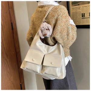 Detail of a beige tote bag with two front pockets and a cute grey plush bunny charm