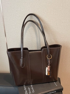 Dark brown glossy leather tote bag with vertical stitching and bohemian beaded charm