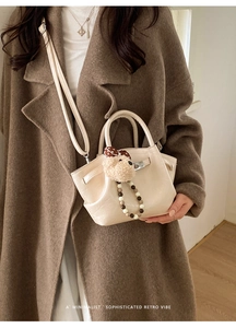 Sac seau beige avec breloque ours et chaîne à perles sur un manteau en laine marron