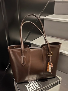 Dark brown faux leather tote bag with ethnic wood bead charm on grey stairs