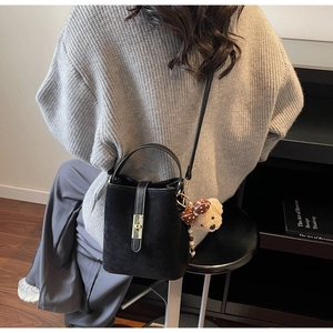 Detail of vintage black bucket bag with gold metal lock and cute bear charm decor