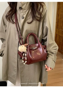 Sac seau rouge foncé avec texture plissée et breloque peluche sur un trench-coat kaki