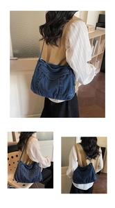 Detail of a large dark blue denim crossbody tote bag with embroidered logo lettering
