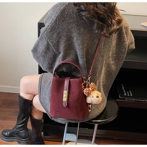 Detail of burgundy frosted bucket bag with gold clasp and teddy bear charm on model
