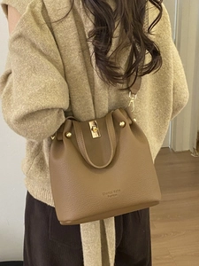 Brown lychee leather bucket bag with gold hardware shown as a crossbody on model