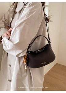 Detail of a brown leather shoulder bag with vintage beads on a beige trench coat