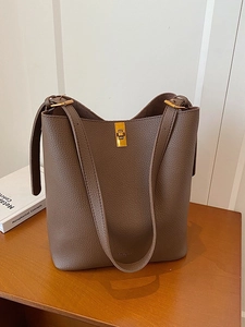 Brown lychee leather bucket bag with gold lock and shoulder strap on a wooden table