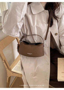 Detail of dark brown lychee leather crossbody bag with wooden bead charm and white text