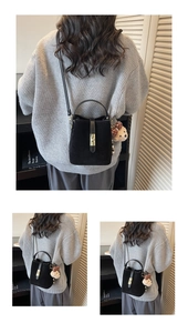 Detail of black matte bucket bag featuring golden twist lock and brown teddy bear charm