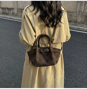 Détail du sac seau en daim marron foncé avec motifs matelassés et finitions dorées