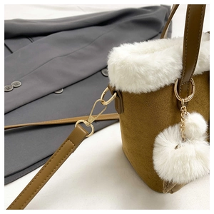 Detail of brown suede handbag featuring white faux fur trim and plush ball pendant
