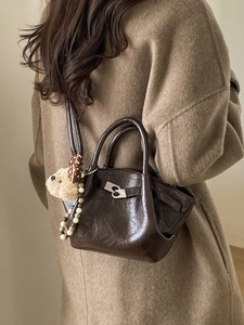 Sac seau marron en cuir poli avec breloque ours et sangle perlée porté par un mannequin