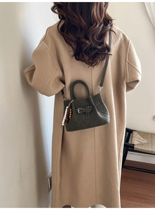 Detail of dark green V-quilted handbag with wood bead charm on a beige coat model