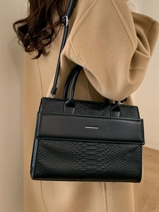 Black faux crocodile texture tote bag with silver logo text shown on a camel wool coat