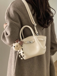Sac seau crème avec breloque ours et chaîne perlée porté sur un manteau en laine marron