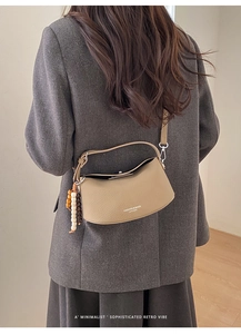 Detail of a crescent leather crossbody bag with wooden bead charm on a grey coat