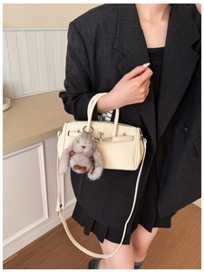 Detail of cream lychee texture bag with a cute plush rabbit charm and gold-tone hardware