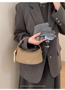 Detail view of khaki leather half-moon handbag with beaded charm and logo on a chic suit