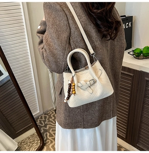 Detail view of cream handbag with V-shaped quilting, wooden beads, and crossbody strap