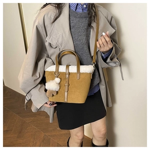 Detail of brown suede tote bag with white faux fur trim and plush ball accessory