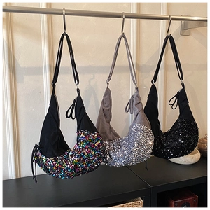 Three sequined crescent bags in black, silver, and grey on a retail store display rack