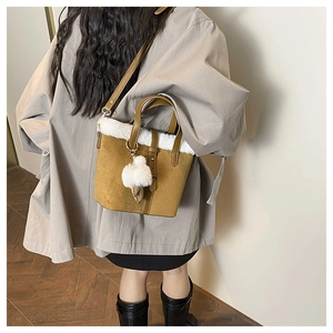 Model wearing a mustard yellow suede bucket bag with white plush trim and pompom detail