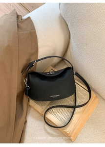 Detail of black lychee grain leather handbag featuring a silver twist lock on yellow books