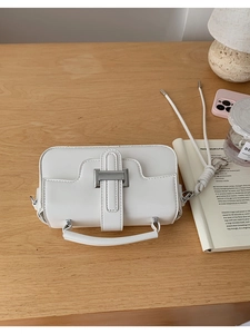 Macro shot of white leather crossbody bag with silver metallic buckle on a wooden desk